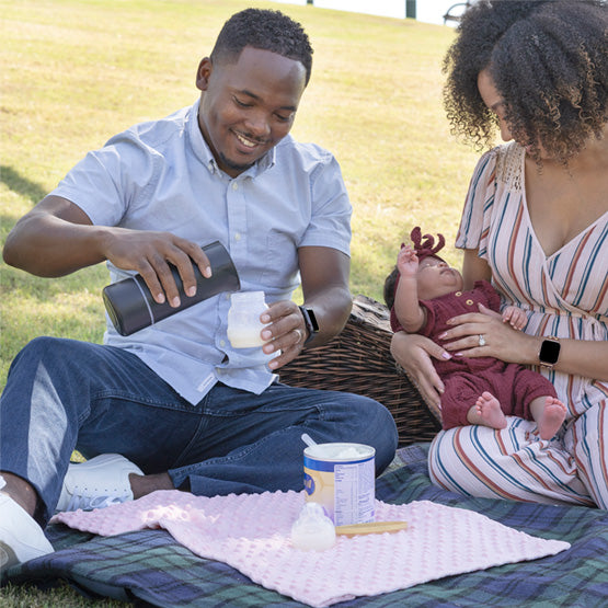 Family using the BisbeeBaby Keddle cordless portable bottle warmer during a picnic, warming milk for their baby while feeding outdoors.