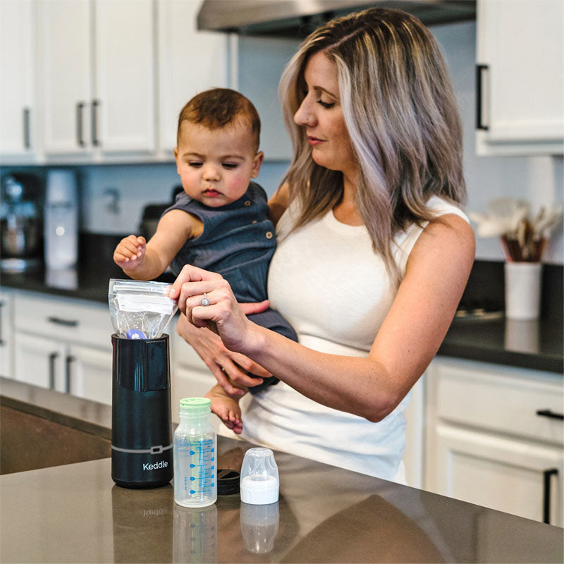 The Keddle portable breast milk bottle warmer sitting next to mom feeding baby in nursery.