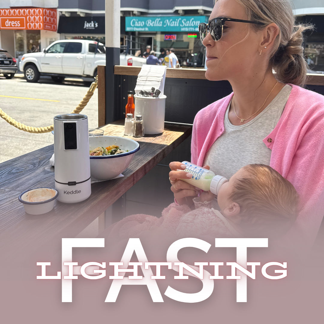 Parent feeding a baby at an outdoor café using the BisbeeBaby Keddle cordless portable bottle warmer to quickly warm milk while on the go.